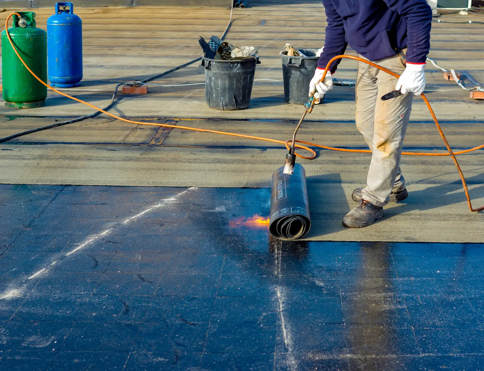 Roofer laying torch-on felt across a large flat roof