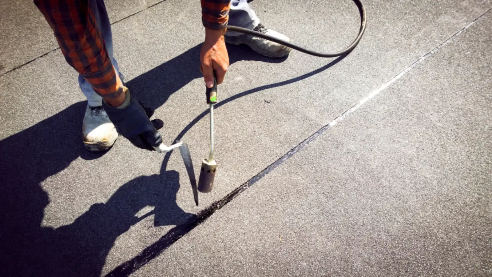Roofer sealing a seam on a mineral felt flat roof with a gas torch and trowel