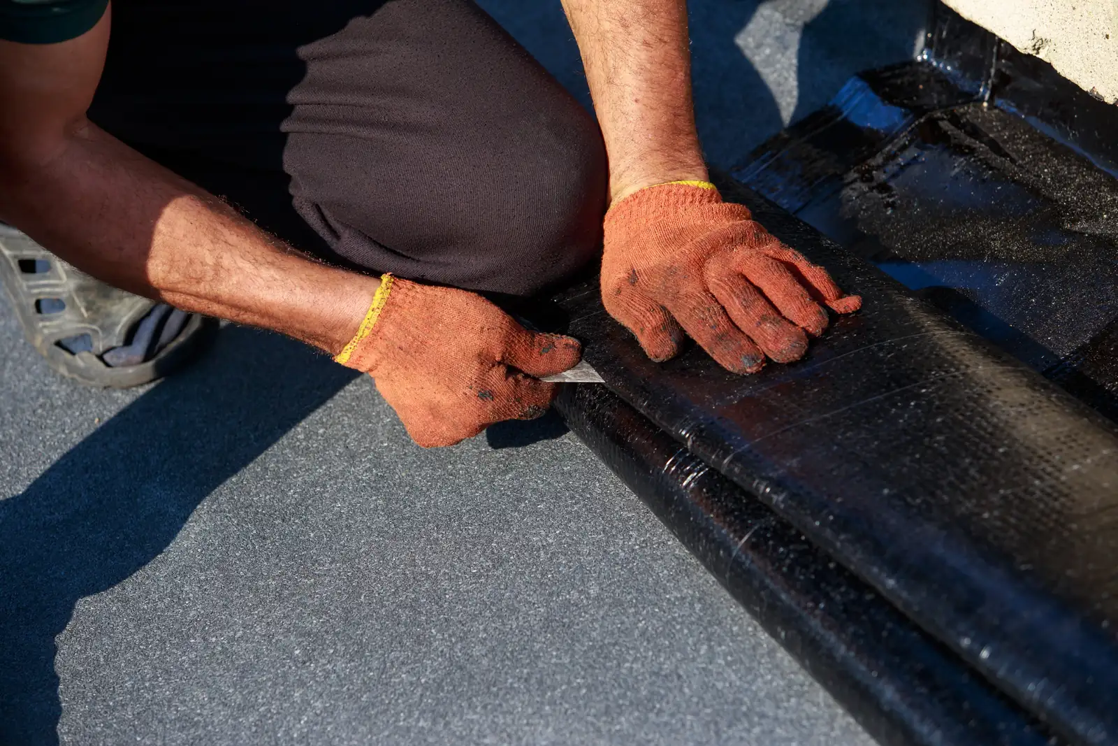 Roofer cutting and dressing felt at an upstand where a flat roof meets a wall