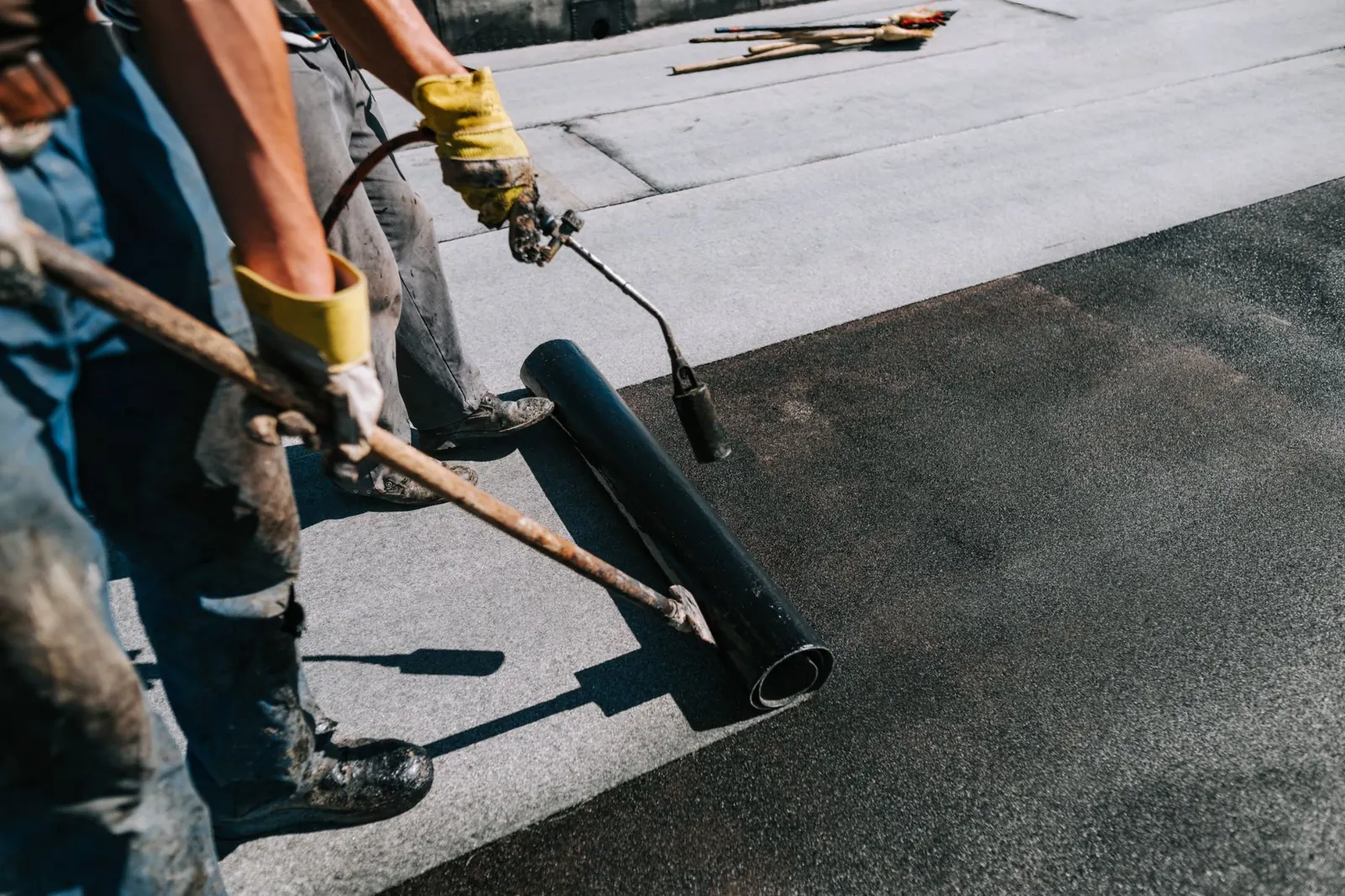 Roofers rolling out torch-on felt and heat-bonding it to a flat roof with a gas torch